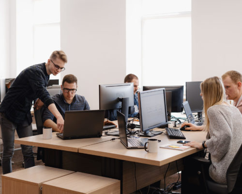 Full concentration at work. Group of young business people working and communicating while sitting at the office desk together with colleagues sitting in the background